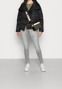 Czarna kurtka puchowa z dużym kołnierzem, zestawiona z zieloną bluzką, szarymi ubraniami skinny jeans i białymi sneakersami. Zawiera również małą torbę na ramię.