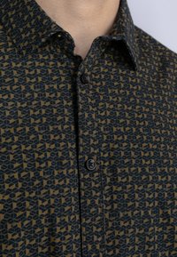 Camicetta a maniche corte in blu scuro e beige con motivo a cubi geometrici. Presenta un collo classico e chiusure con bottoni neri.