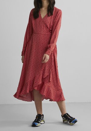 Robe portefeuille rouge à fleurs avec des manches longues, un ourlet volanté et une texture douce, associée à des baskets de sport noires et bleues.