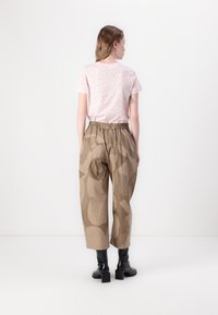 Light pink t-shirt with floral print, paired with textured brown trousers featuring abstract patterns and elastic waist, worn with black boots.