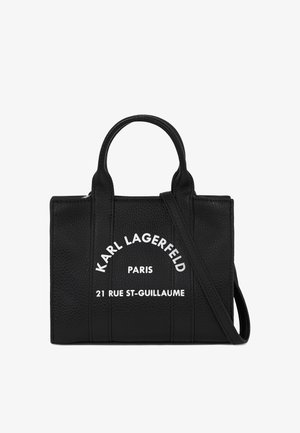 Bolso de mano de cuero negro con superficie texturizada. Cuenta con dos asas superiores y una correa desmontable. Texto blanco que muestra la marca y la información de la dirección.