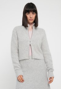 Cardigan corto grigio chiaro realizzato in un morbido tessuto testurizzato, con colletto alto, maniche lunghe e zip bidirezionale.