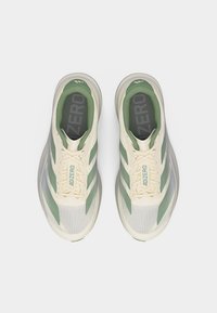 Ζευγάρι από κρεμ και πράσινα παπούτσια Adidas Adizero για τρέξιμο με κορδόνια, σε θέα από πάνω σε λευκό φόντο.