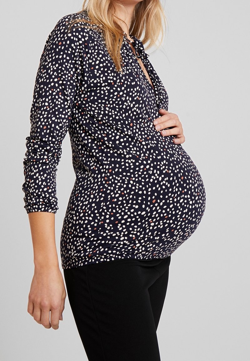 Graviditetstopp i marinblått med vitt och rött mönster. Långa ärmar, avslappnad passform, veckade sidor för komfort över en rundad mage.