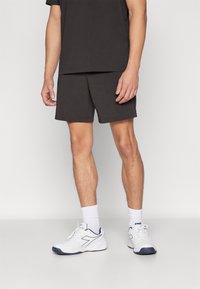Svart bomull T-skjorte og matchende shorts, med hvite joggesko med marineblå detaljer og hvite ankelstrømper. Enkel, avslappet design.