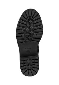 Suela de zapato de goma negra con un dibujo texturizado y un patrón múltiple que presenta surcos pronunciados y perforaciones circulares. Logo de la marca visible.