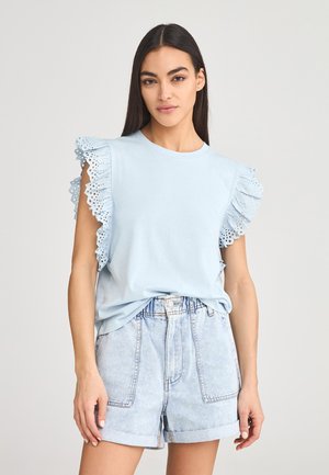 T-shirt azzurro chiaro con maniche a volant in pizzo, tessuto morbido, scollatura rotonda, abbinato a pantaloncini di jeans chiari a vita alta.