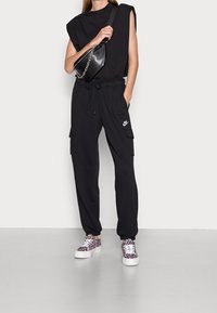 Svart ärmlös topp, svarta cargobyxor med fickor, och vita sneakers med rosa leopardmönster. Svart axelväska med kedjeslang.