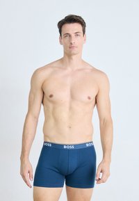 Navy blue boxer shorts with a soft texture, featuring a wide white waistband with the "BOSS" logo. Slim fit design, minimal seams.