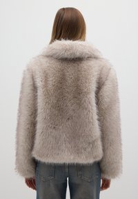 Nepbontjas in lichtbeige, met een brede kraag, lange mouwen en een boxy silhouet van textuurrijk pluche materiaal.