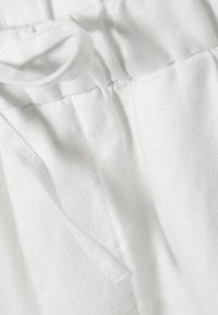 Nahaufnahme eines weißen Stoffes mit einer genähten Naht und einer Kordelschlaufe, die Textur- und Nähdetails zeigt.