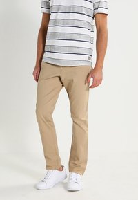 Beige chinos, triko s šedými a bílými pruhy a bílé tenisky. Bavlněný materiál, volný střih a krátké rukávy s detailním štítkem.