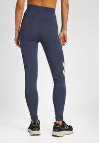 Marina leggings med hög midja, tillverkade av mjukt tyg, med en grå zigzag-design på sidan, tillsammans med svarta sneakers.