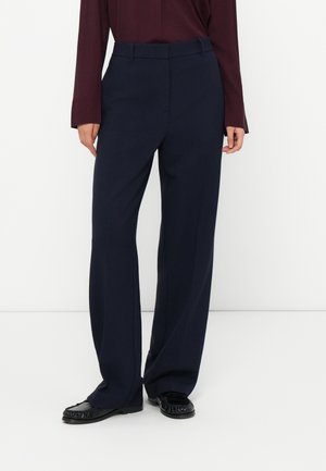 Person wearing navy wide-leg trousers, black moccasin shoes, and a burgundy long-sleeve top standing against a white background.