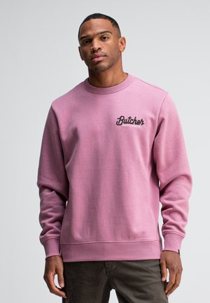 Roze sweatshirt met geribbelde halslijn en manchetten, met een zwart geborduurd "Butcher" logo op de borst. Zachte stof en een ontspannen pasvorm.