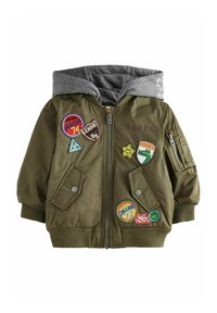 Veste vert olive avec capuche grise, fermeture éclair et plusieurs patchs colorés; comprend deux poches avant et des poignets côtelés.