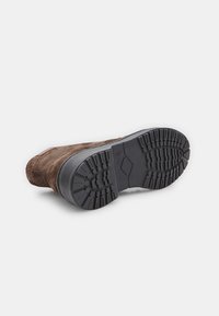 Bota de ante marrón con suela de goma negra texturizada que presenta un patrón de relieve resistente para una mayor tracción y durabilidad.