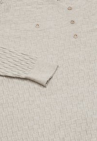 Beżowy sweter dziany z textured wzorem, z dekoltem w serek, trzema dekoracyjnymi guzikami oraz ściągaczami na długich rękawach.