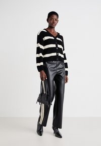 Zwart-wit gestreepte cardigan met knopen, gecombineerd met hoge zwarte faux leren broeken en puntige enkellaarsjes met stippen.