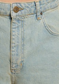 Jeans de denim azul claro con cremallera y cierre de botón de metal, que presentan costuras naranjas y un detalle en el bolsillo delantero.