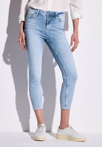 Jean en denim bleu clair avec une taille haute, un fit cropped et un léger délavage. Associé à des baskets blanches.