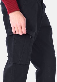 Pantaloni cargo neri realizzati in tessuto resistente, dotati di tasche laterali con chiusura a scatto e un design leggermente affusolato.