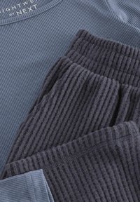 Grau gerippter Lounge-Set aus weichem, strukturiertem Stoff. Besteht aus einem hellblauen Oberteil mit glatter Oberfläche und rundem Halsausschnitt.