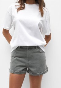 Camiseta blanca de algodón con mangas cortas, combinada con pantalones cortos de denim gris, con dobladillo deshilachado y bolsillos frontales, diseño ajustado.