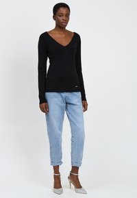 Schwarzer V-Ausschnitt-Pullover, taillierte Passform, leichtes Material. Kombiniert mit hellblauen, hochgekrempelten Jeans und silbernen Glitzer-Pumps.