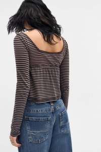 T-shirt de manga longa listrado em castanho e cinza com um recorte quadrado nas costas, combinado com jeans azul de cintura alta com bolsos traseiros.