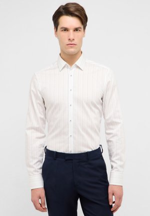 Chemise blanche à manches longues avec des rayures verticales pastel. Elle présente un col pointu, une fermeture boutonnée et des accents de boutons contrastants.