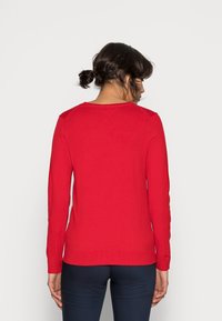 Pull rouge à manches longues avec texture côtelée et encolure ronde. Présente une coupe ajustée et une couleur unie, sans motifs ni logos visibles.