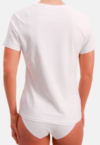 Biała bawełniana koszulka z krótkimi rękawami, okrągłym dekoltem i gładką fakturą, widok od tyłu; w komplecie z białymi szortami.