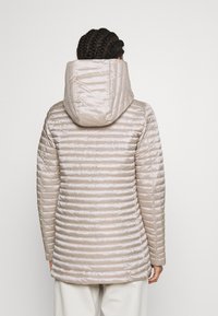 Jasny beżowy, pikowany płaszcz z poziomym przeszyciem, dopasowanym krojem i dużym kapturem. Materiał wydaje się błyszczący i gładki, odpowiedni na chłodniejszą pogodę.