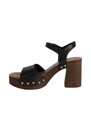 Zwarte leren platform sandaal met een brede band, enkelband en een blokhak. Gouden studs versieren de zijkant van de schoen voor extra detail.