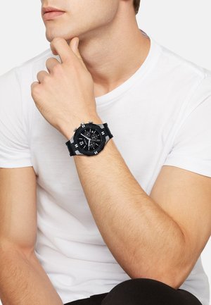 Sort kronograf ur med en struktureret sort gummirem og en sort urskive med sølv detaljer og store timemarkører.