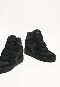 Sneakers alte nere realizzate in suede e rete, dotate di tre cinturini in Velcro regolabili e un tacco a zeppa. Suola in gomma nera texturizzata.