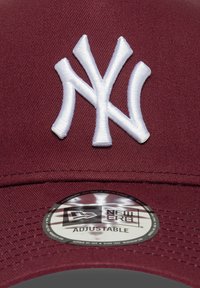 Bordo bejzbol kapa s podesivim remenom, s bijelim izvezenim NY logom i okruglim New Era naljepnicom na rubu.