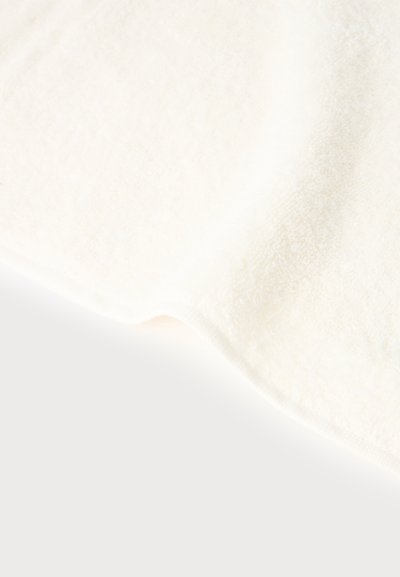 Gros plan d’un tissu polaire blanc et doux, avec un bord légèrement incurvé et une surface texturée, sur un fond clair et uni.