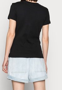 Černé bavlněné tričko s krátkým rukávem a kulatým výstřihem. V kombinaci se světlými džínovými šortkami, které mají ohrnuté nohavice a zadní kapsy.