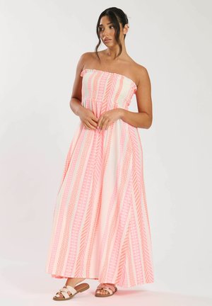 Strapless maxi-jurk met roze en witte verticale strepen, voorzien van geometrische patronen. Soepele stof, vloeiende snit en eenvoudige sandalen.