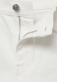 Tela de mezclilla blanca con un zipper de metal parcialmente desabrochado y un cierre de botón plateado. Presenta detalles de costura a lo largo de los bordes.