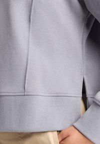 Ljusgrå sweatshirt med ribbade ärmslut och nederkant, med en sidöppning. Mjuk, slät textur med en avslappnad passform.