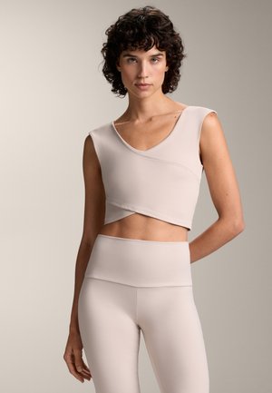 Béžový sportovní crop top s výstřihem do V a krátkými rukávy, s volným designem. V kombinaci s vysokými legínami ve stejném stylu.