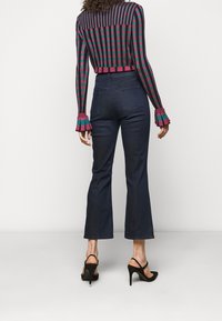 Pantalones de mezclilla oscuros, ajustados y acampanados con cintura alta, combinados con una blusa de manga larga de rayas multicolor y zapatos de tacón negro.