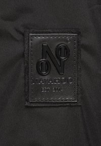 Black fabric tag with embossed text "NAVAHOO" and "EST 2014," featuring a stylized "N" and circular accent, stitched around the edges.