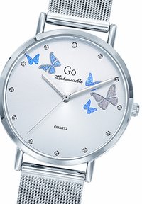 Montre en quartz argentée avec bracelet en mailles, affichant un cadran minimaliste, des motifs de papillons bleus et métalliques, et des index horaires en cristal.
