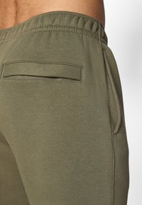 Calças jogger verde-azeitona feitas de tecido macio, com cintura elástica, bolso lateral e um pequeno bolso nas costas.