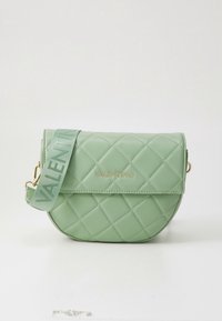 Zelená prošívaná kabelka s zakřiveným tvarem, zlatým kováním a páskem s logem. Vyrobena z hladkého materiálu, má klopové zapínání.