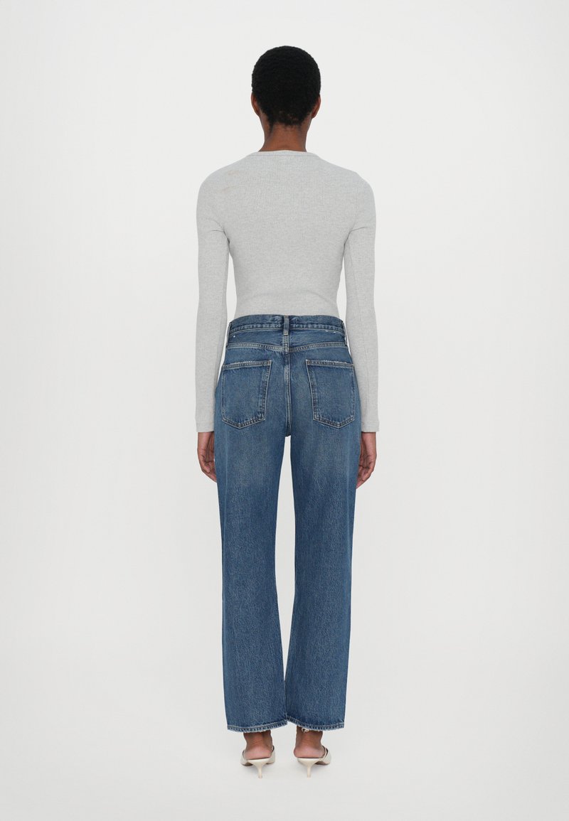 Gray long-sleeve top paired with high-waisted, wide-leg blue denim jeans. The jeans feature two back pockets and a raw hem.
